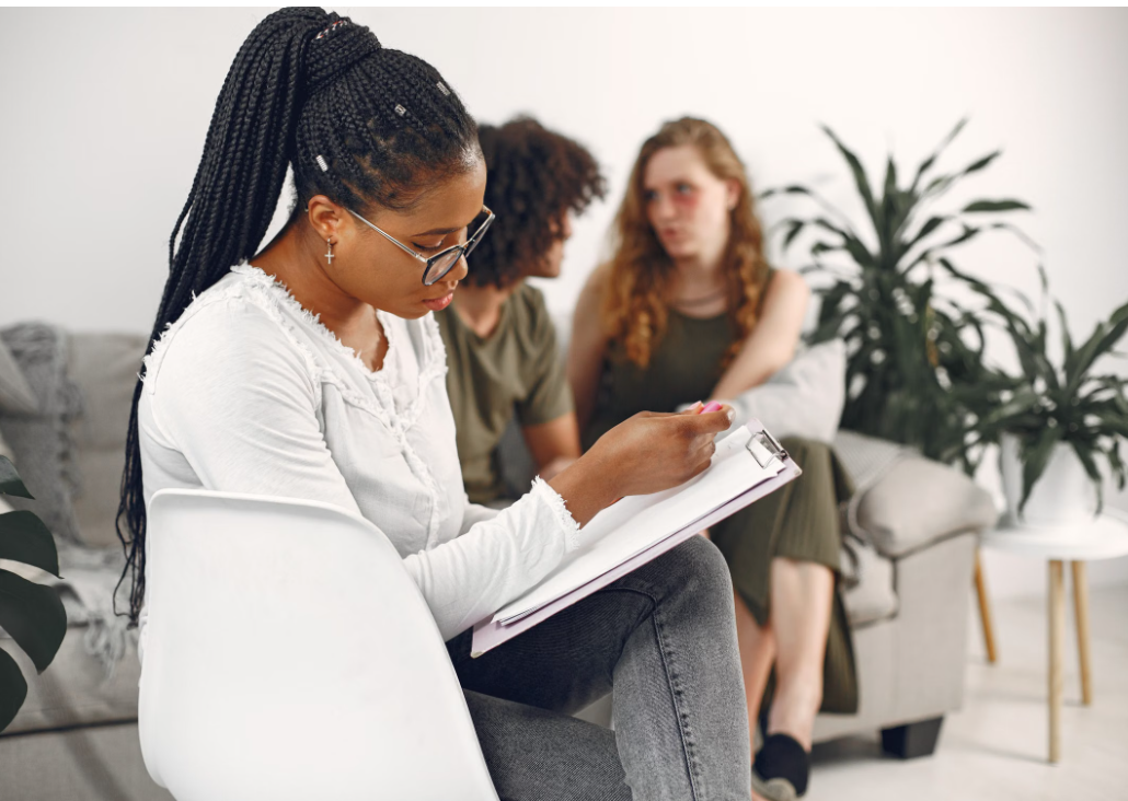 A Black counselor taking notes while a couple talks together during a counseling session