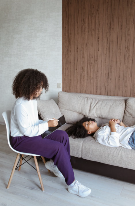 A Black woman resting on a couch while talking with her counselor in a calm, bright office